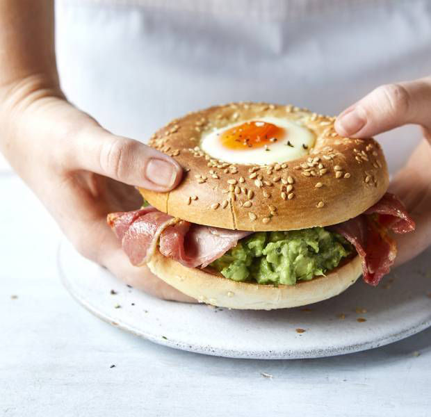 Bacon and smashed avocado bagel with an egg baked into the top